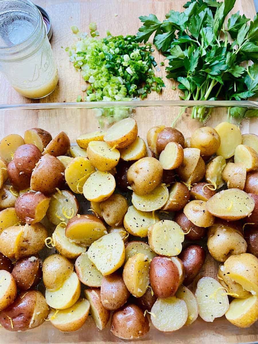 Prepared baby potatoes, jar of dressing, chopped herbs on a wooden cutting board