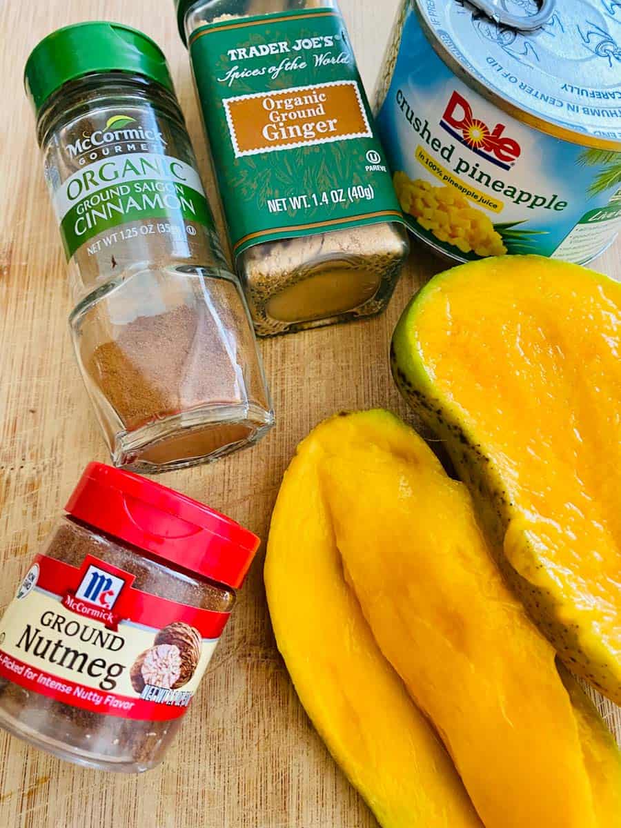 Fresh mango, canned pineapple, and spices laid out on a wooden cutting board