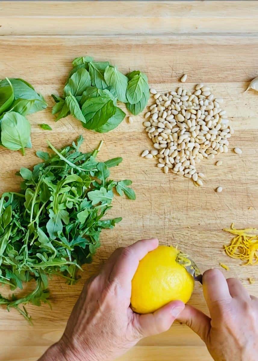 Zesting a lemon and trying not to cut myself, plus mint, basil, arugula, and pine nuts on a cutting board
