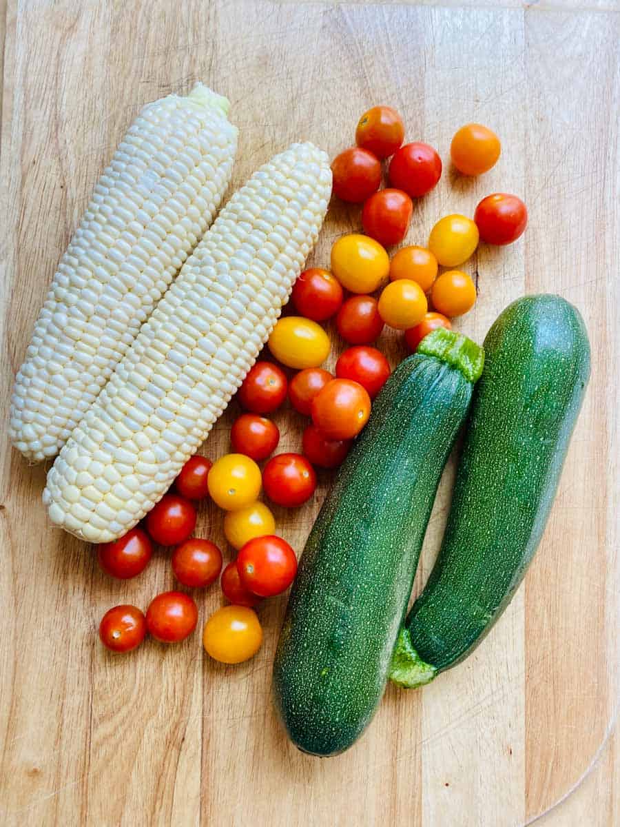 Two ears of corn, two zucchini, and a mess of itty bitty grape tomatoes in red, yellow, and orange
