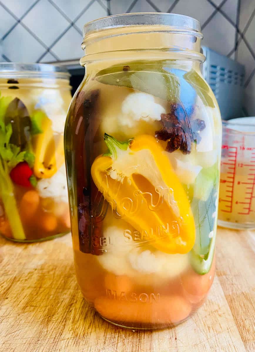Carrots, cauliflower, celery, and bell peppers cut up and in a mason jar with spices and vinegar brine. Also called escabeche.