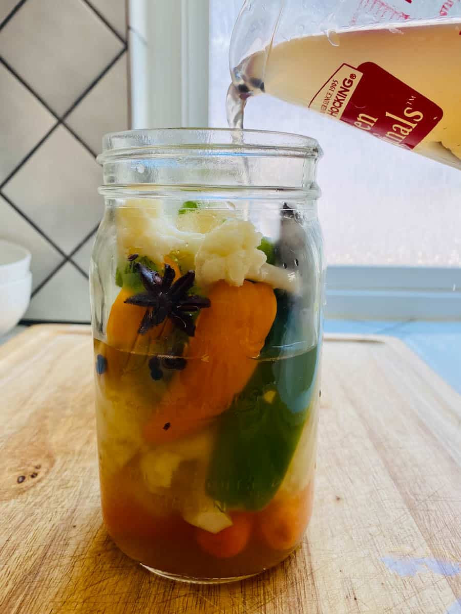 Side view of escabeche in a mason jar with hot vinegar brine being poured into it