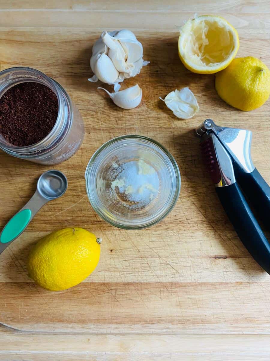 Ingredients for sumac dressing: lemon, garlic, salt, and sumac laid out on a wooden board