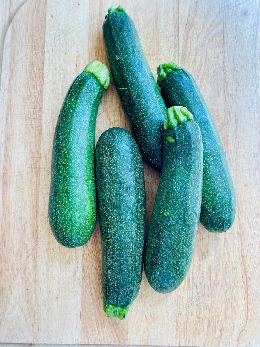 Five whole zucchini piled on a wooden cutting board