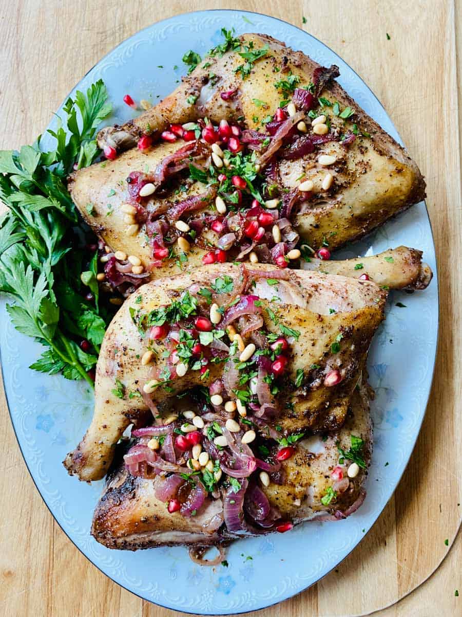 Roasted chicken with sumac on a platter and topped with parsley, pine nuts, and pomegranate.