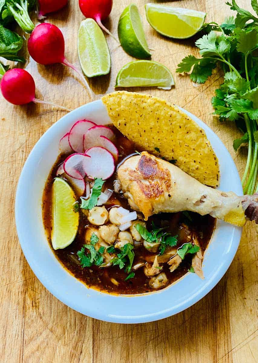 Pozole with Chicken in a bowl and surrounded by radish, limes, and cilantro.