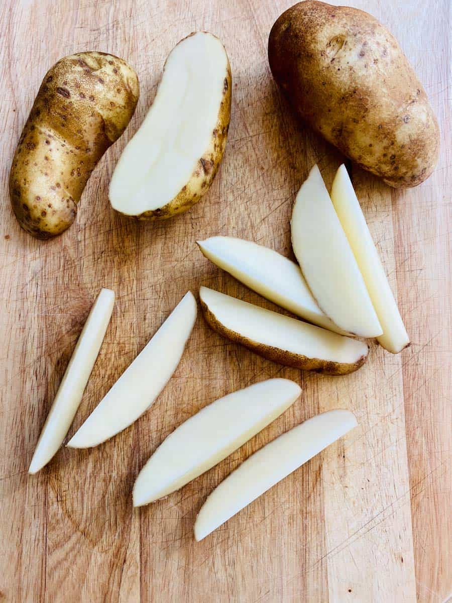 Russet potatoes being cut into wedges for the sheet pan.