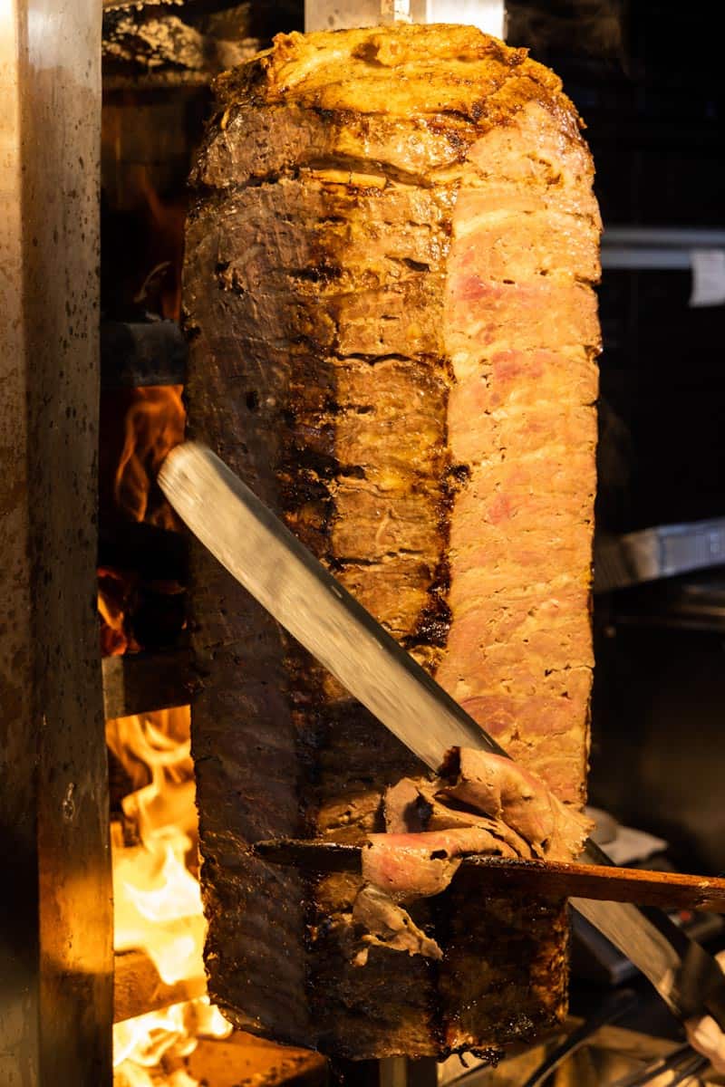 Doner kebab meat being sliced from a vertical rotisserie.