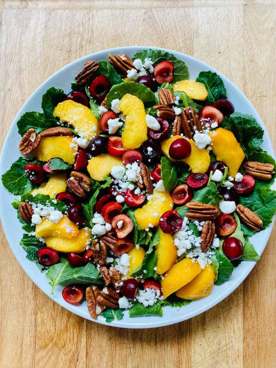Kale salad assembled with cherries, peaches, pecan, and goat cheese.
