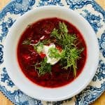 Bowl of borscht topped with sour cream and fresh dill.