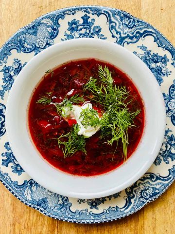 Bowl of borscht topped with sour cream and fresh dill.