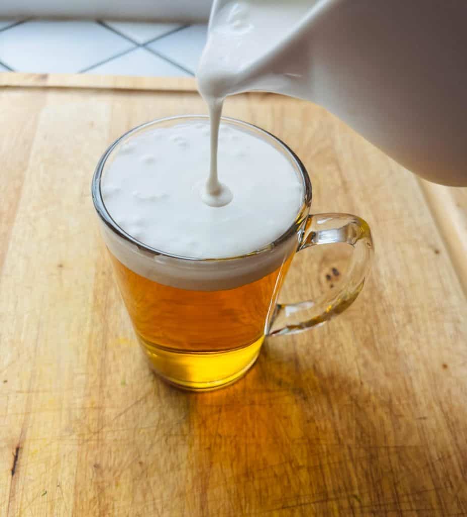 Pouring the cream on top of hot apple cider.