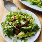 Arugula endive salad with bacon being drizzled with vinaigrette.