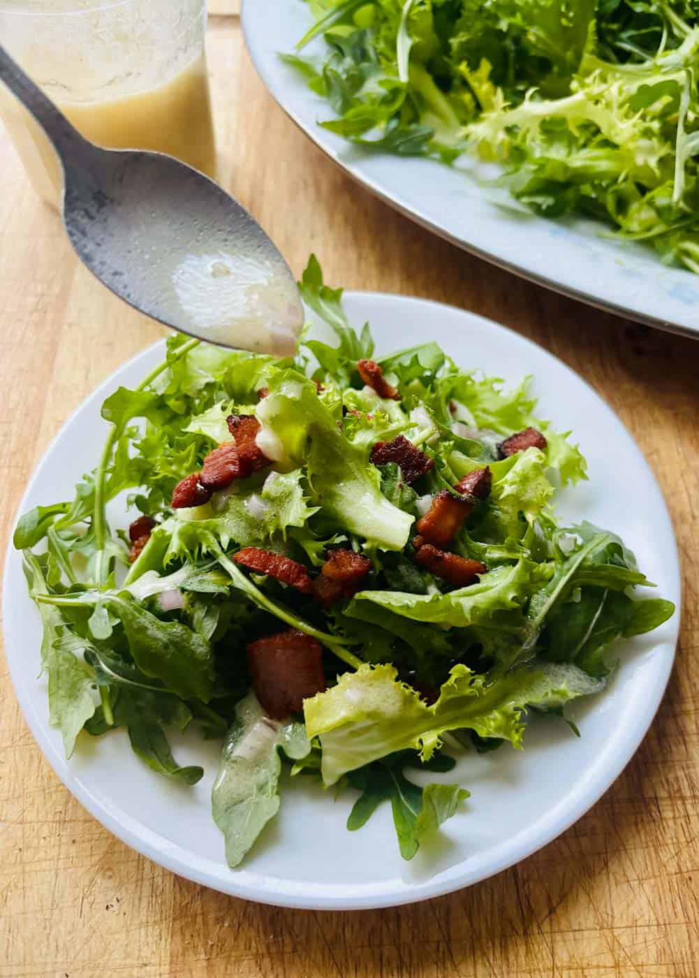 Arugula endive salad with bacon being drizzled with vinaigrette.
