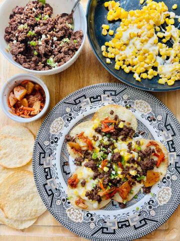 Korean Nachos assembled with crispy chips, kimchi, ground beef, and cheesy corn.