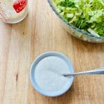 Caesar salad dressing in a ramekin, extra dressing, and shredded romaine lettuce.