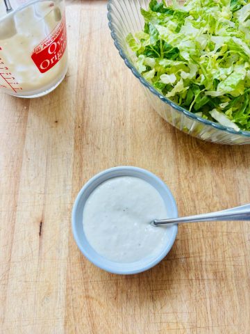 Caesar salad dressing in a ramekin, extra dressing, and shredded romaine lettuce.