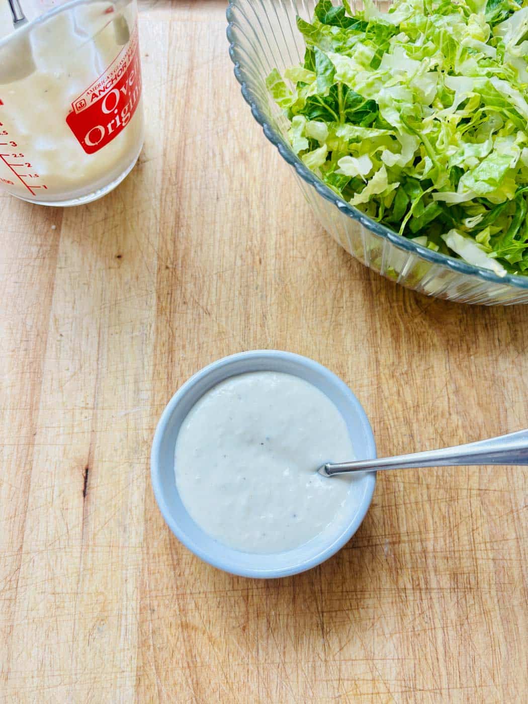 Caesar salad dressing in a ramekin, extra dressing, and shredded romaine lettuce.