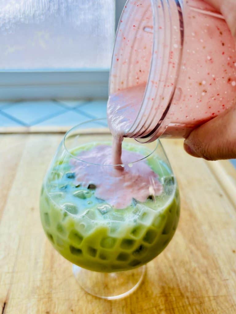 Pouring strawberry cold foam onto matcha latte.